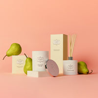 Elegant display of French Pear scented products, including a candle and diffuser, with fresh pears on a soft peach background. Calm, luxurious atmosphere.