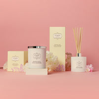 Elegant display of a Sweet Pea and Jasmine candle and diffuser set against a soft pink background, accented with white flowers, conveying calm and luxury.