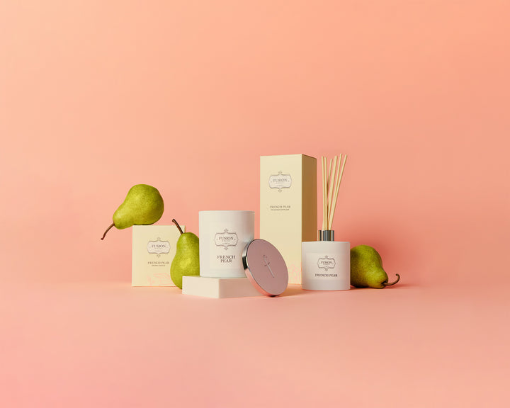 A decorative scene of French Pear Soy Candle and Fragrance Diffuser with Green Pears surround them against a pink background