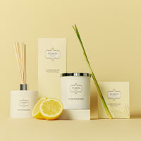 A colourful display featuring a lemon, shallot, a white glass jar candle, and a glass diffuser jar, highlighting a selection of diverse products on a muted yellow background.